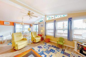 A living room with a ceiling fan, a yellow sofa, a green chair, a patterned rug, and a bookshelf. - Canal front home with free WiFi, deck, private dock, shared pool & tennis (Ocean City)