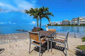 A wooden deck with a table and chairs, palm trees, and a view of the ocean and buildings. - Sunlit island abode with bayside beach, pools, WiFi, balcony, & AC (Ocean City)