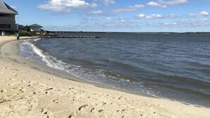 Ein Strand mit einem Gebäude, blauem Himmel und ruhigem Wasser.