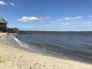 Ein Strand mit einem Gebäude, blauem Himmel und ruhigem Wasser.