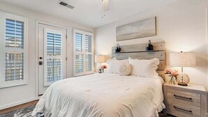 Ein Schlafzimmer mit einem großen Bett, einem Deckenventilator, einem Nachttisch mit Lampe und einem Fenster mit Jalousien.