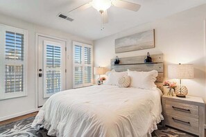 Ein Schlafzimmer mit einem großen Bett, einem Deckenventilator, einem Nachttisch mit Lampe und einem Fenster mit Jalousien.