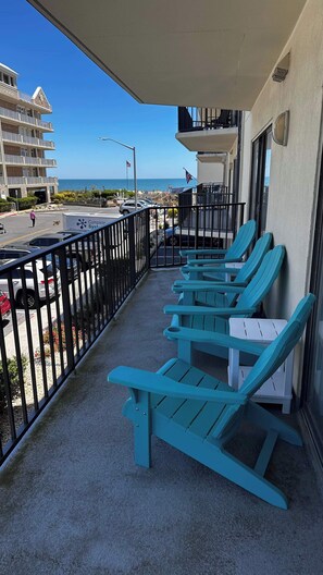 A balcony with teal lounge chairs, a view of the ocean, and a building with balconies. - Royal Hawaiian 106 (Ocean City)