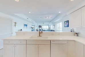 A modern kitchen with a large island, white cabinetry, and a built-in dishwasher. - Sunset Pointe 206 (Ocean City)