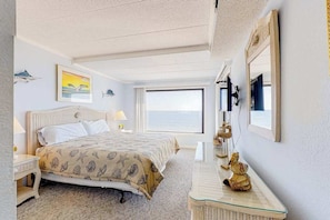 A bedroom with a bed, a bedside table, a lamp, a window, and a wall-mounted mirror. - Sixth floor oceanfront condo with beach access (Ocean City)