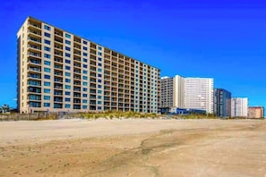 A multi-story hotel with a uniform facade, balconies, and a clear sky. - Sixth floor oceanfront condo with beach access (Ocean City)