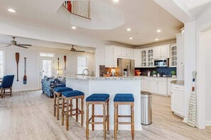 A modern kitchen with white cabinets, a central island with stools, and a stainless steel refrigerator. - Sunset Island - 59 Island Edge (Ocean City)