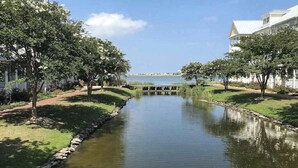 A serene waterway flanked by trees and a bridge, leading to a distant shoreline. - Sunset Island - 59 Island Edge (Ocean City)