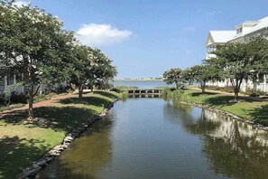 A serene waterway flanked by trees and a bridge, leading to a distant shoreline. - Sunset Island - 59 Island Edge (Ocean City)