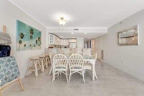 Ein geräumiger Essbereich mit weißen Stühlen und einem Tisch, im Hintergrund eine Küche und ein Gemälde an der Wand.