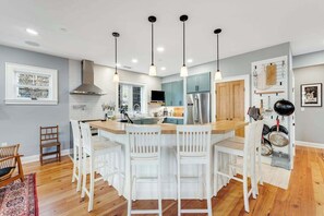 A modern kitchen with a central island, white bar stools, pendant lighting, and a built-in stove. - Canal-front getaway with private hot tub, large deck & firepit - dog-friendly (Ocean City)