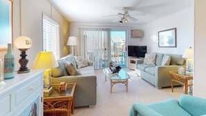 Ein Wohnzimmer mit Deckenventilator, zwei Sofas, einem Fernseher und einem Glastisch.