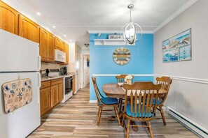 Eine Küche mit Holzsäulen, einem weißen Kühlschrank, einer blauen Wand mit einer Uhr und einem Esstisch mit Stühlen.
