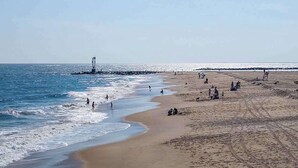 A beach with a lighthouse, sandy shore, and people. - Blue Marlin 402 (Ocean City)