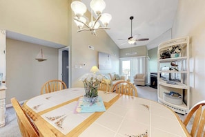 A dining area with a wooden table, chairs, a chandelier, and a bookshelf. - Blue Marlin 402 (Ocean City)