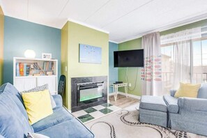 A living room with a fireplace, a flat-screen TV, a bookshelf, and a sofa. - Summer Palace 7 (Ocean City)