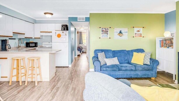 Una cucina moderna con mobili bianchi, un'isola centrale con sgabelli e un divano blu in un soggiorno dalle pareti verdi.