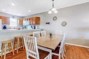 A kitchen with wooden cabinets, a dining table with chairs, and a hanging light fixture. - Captain's View 2 (Ocean City)