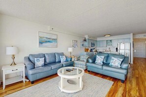 Ein Wohnzimmer mit einem blauen Sofa, einem Couchtisch und einer Küche im Hintergrund.