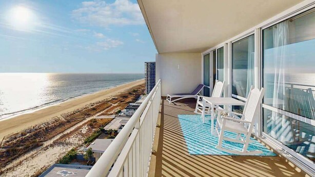 Un balcón con vista a la playa, sillas blancas y una alfombra azul.