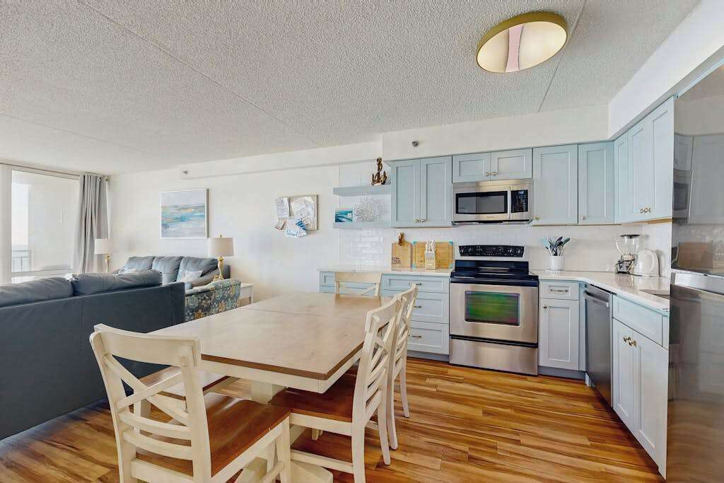 A modern kitchen with light blue cabinets, a wooden dining table, and a built-in oven.
