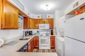 A compact kitchen with wooden cabinets, a white stove, a microwave, and a refrigerator. - Beach & Bright Oceanfront Condo W/ Fast WiFi, Patio, Beach Access & More (Ocean City)
