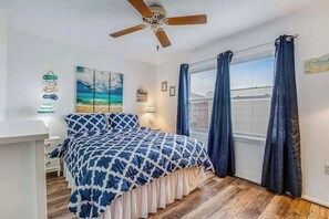 A bedroom with a bed, a ceiling fan, a window with curtains, and wall decorations. - Beach & Bright Oceanfront Condo W/ Fast WiFi, Patio, Beach Access & More (Ocean City)