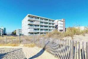 A multi-story hotel with balconies, a sandy beach in the foreground, and a clear blue sky. - Oceanfront Condo with Balcony, Sunrise Views, Free WiFi & Washer/Dryer (Ocean City)