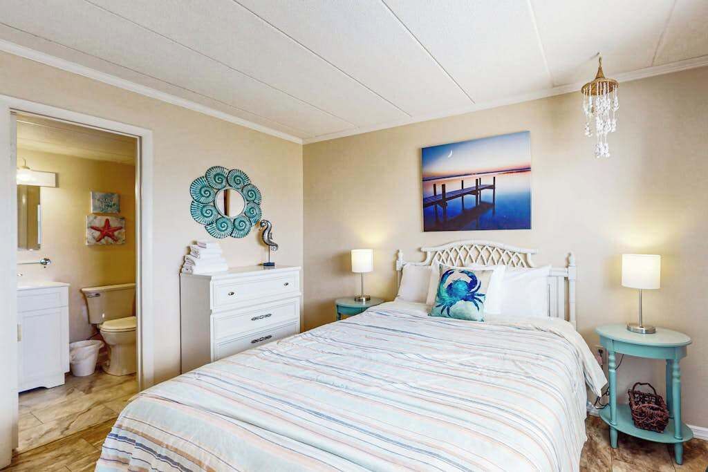 A bedroom with a bed, a nightstand, a dresser, a bathroom, and a wall with a painting.
