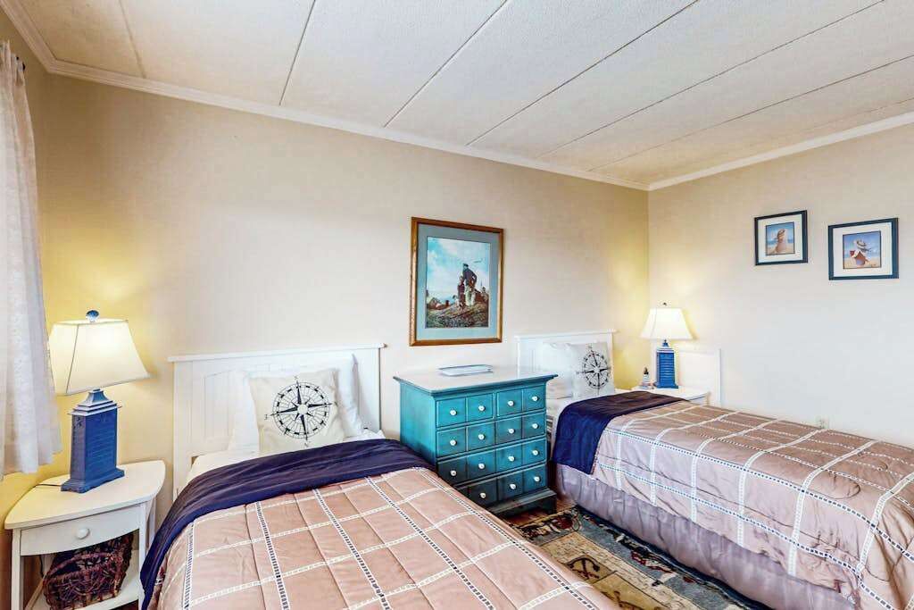 A bedroom with two beds, a dresser, and a painting on the wall.