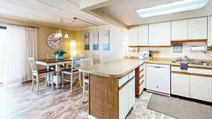 A modern kitchen with a central island, white cabinetry, and a dining area with a wooden table and chairs. - Ocean Place 519 (Ocean City)