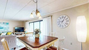 A dining area with a wooden table, chairs, a clock, and a television in the background. - Ocean Place 519 (Ocean City)