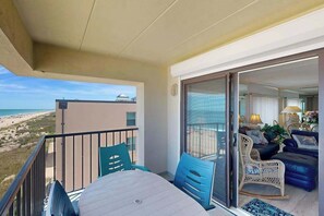 Ein Balkon mit Tisch und Stühlen, Blick auf den Strand und ein Wohnbereich mit Sofa und Lampe.