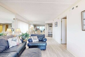 A modern living room with a sofa, armchair, and a coffee table. There is a door leading to another room. - Waikiki 402 (Ocean City)