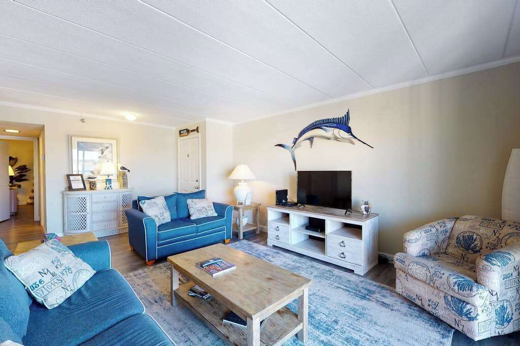 Een woonkamer met een blauwe bank, een houten salontafel, een tv-meubel en gestreept meubilair.