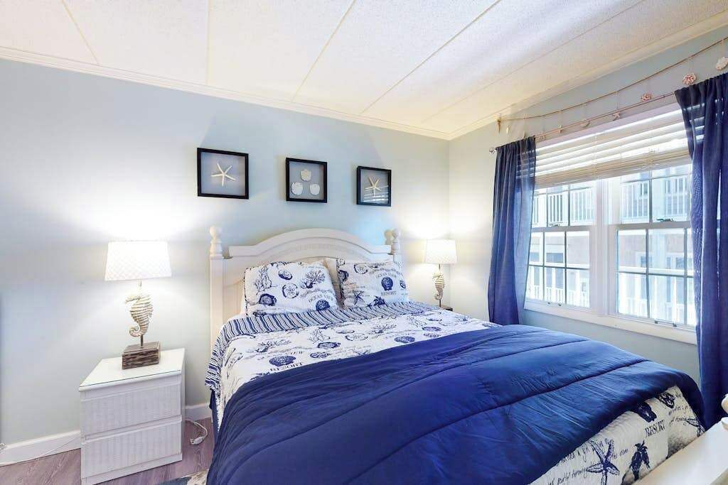 A bedroom with a bed, bedside lamps, a window with curtains, and framed pictures on the wall.