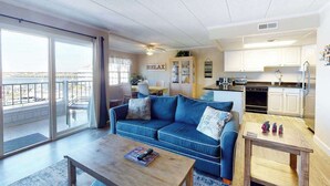 Een woonkamer met een blauwe bank, een bijzettafeltje en een uitzicht door grote glazen deuren op een balkon.