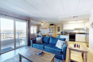 A living room with a blue sofa, a coffee table, and a view through large glass doors to an outdoor balcony. - Charming bayfront condo in Old Town with balcony, WiFi, AC, & shared pool (Ocean City)
