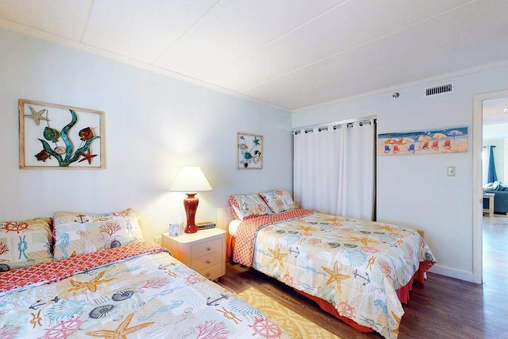 A bedroom with two beds, a nightstand, and a lamp.