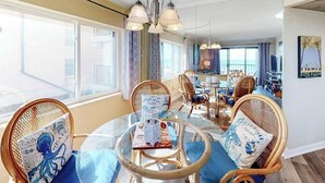 A dining area with wicker chairs, a glass table, and a view of the sea. - Waikiki 102 (Ocean City)
