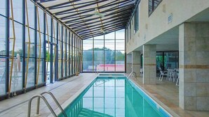 An indoor swimming pool with clear glass walls, a tiled floor, and a covered seating area with tables and chairs. - Waikiki 102 (Ocean City)
