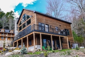A modern two-story wooden cabin with a balcony, surrounded by natural landscape. - Trailside Chalet at Pleasant Mt. (Bridgton)