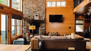 Ein gemütliches Wohnzimmer mit Kamin aus Stein, einer Ledersofa und einem flachbildfernseher an der Wand.