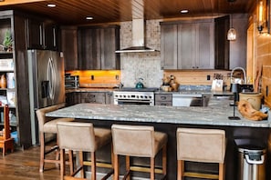 A modern kitchen with a large island, bar stools, stainless steel appliances, and a tiled backsplash. - Trailside Chalet at Pleasant Mt. (Bridgton)