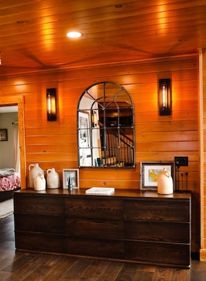 A wooden-paneled room with a dark wooden dresser, a large mirror, and wall-mounted sconces. - Trailside Chalet at Pleasant Mt. (Bridgton)