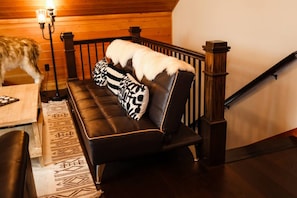 A room with a black leather sofa, patterned throw pillows, a wooden staircase, and a rug with a geometric design. - Trailside Chalet at Pleasant Mt. (Bridgton)