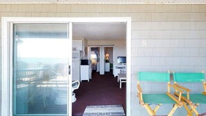 Una stanza con una porta scorrevole in vetro che dà su un balcone, un angolo cottura e una zona salotto con un cuscino verde.
