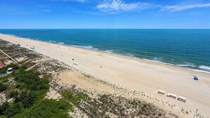 Una spiaggia con un litorale sabbioso, un cielo azzurro limpido e alcune strutture lungo la costa.