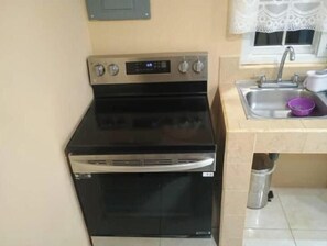 A kitchen with a black stove, a sink, and a window with lace curtains.