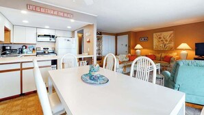 A modern kitchen with white cabinets, a dining table with chairs, a living area with a sofa and lamps, and a ceiling fan. - Thunder Island 28A (Ocean City)